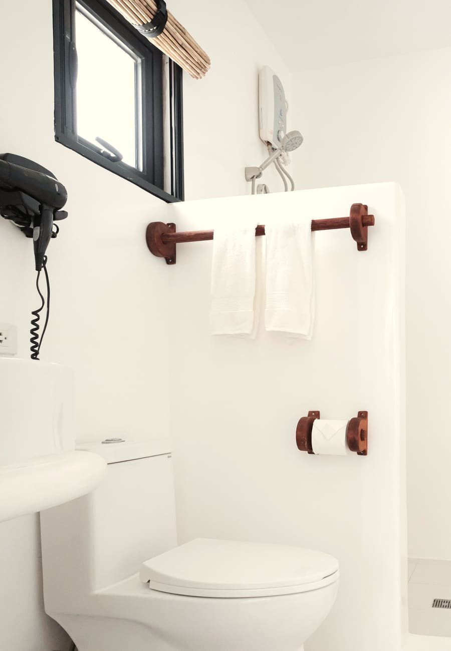 White ensuite bathroom with towels on a wooden rail, a shower, a wall-mounted hair dryer and a small black-framed window.