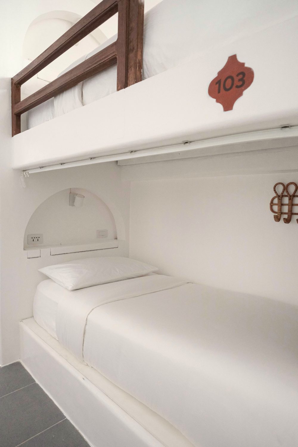 Lower bunk made up with white linen under a wooden rail, with a reading-light niche, sockets and a woven hook; the bunk is numbered 103.