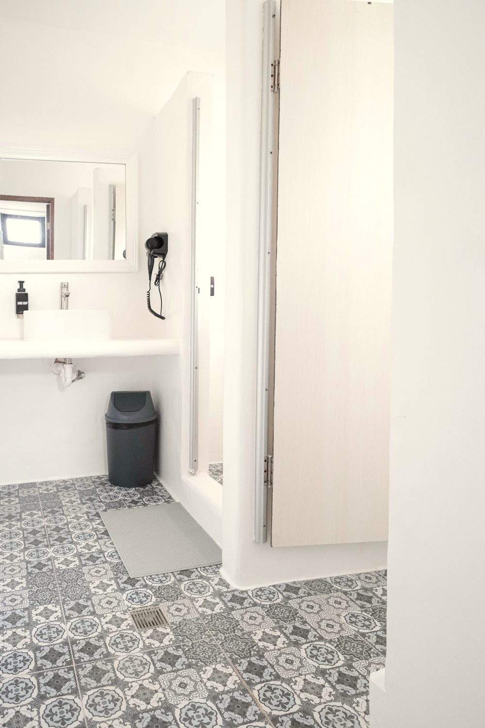 Ensuite bathroom with a white basin, mirror, wall-mounted hair dryer and patterned grey-and-white floor tiles.