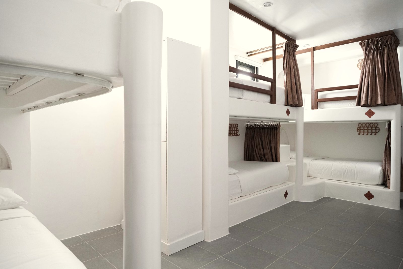 Dorm with white built-in bunks, brown curtains, wooden rails and small steps up to the upper bunks.