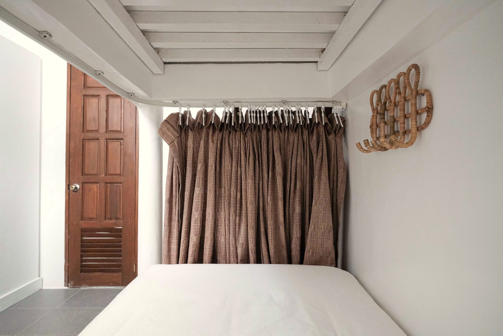 Lower bunk with a brown privacy curtain, a woven hook and a wooden door at the end of the dorm.