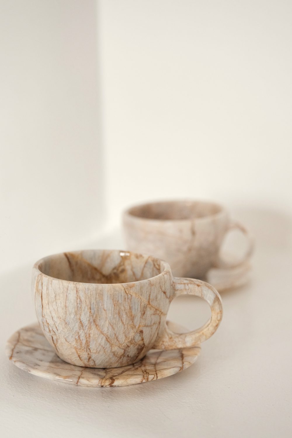 Two marbled ceramic cups and saucers on a white ledge in soft daylight.