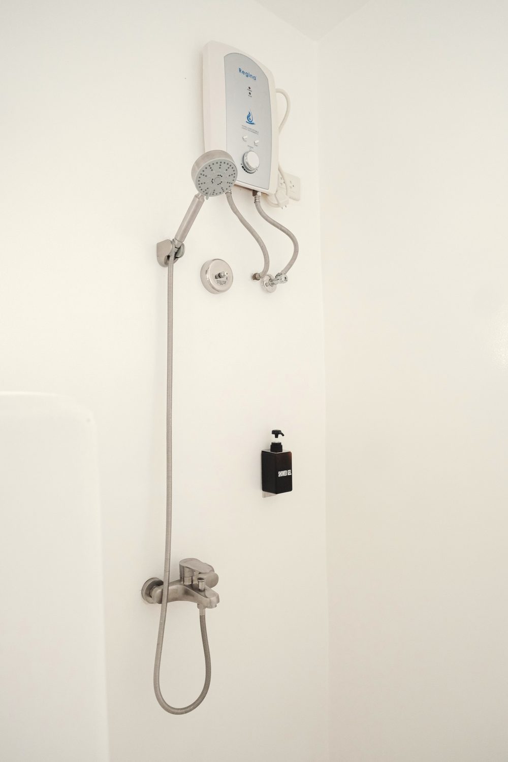 White shower wall with a water heater, a hand shower on a rail and a black soap dispenser.