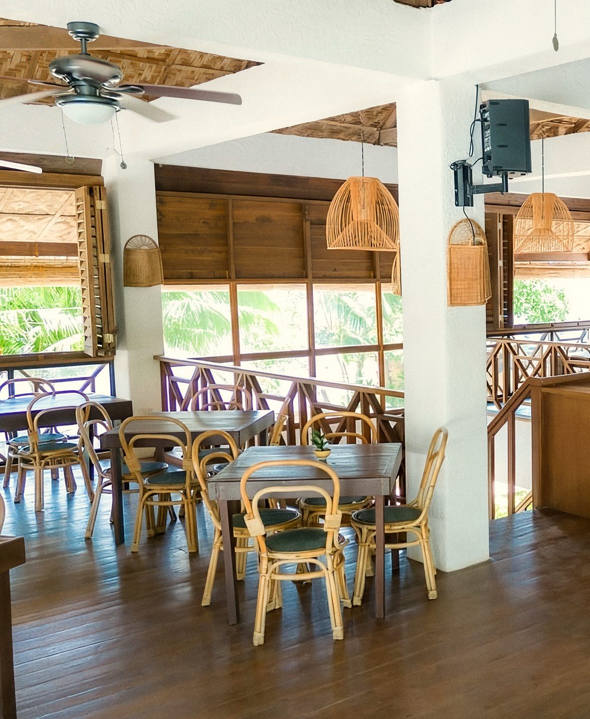 Little Rotti dining room with rattan chairs at wooden tables, woven pendant lamps, a thatched ceiling and open windows onto greenery.