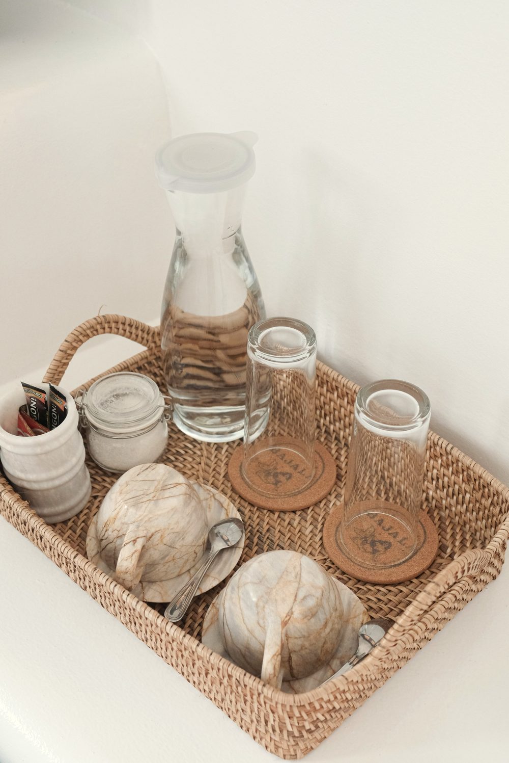 Rattan tray with a glass water carafe, two glasses, marbled cups and wooden coasters.
