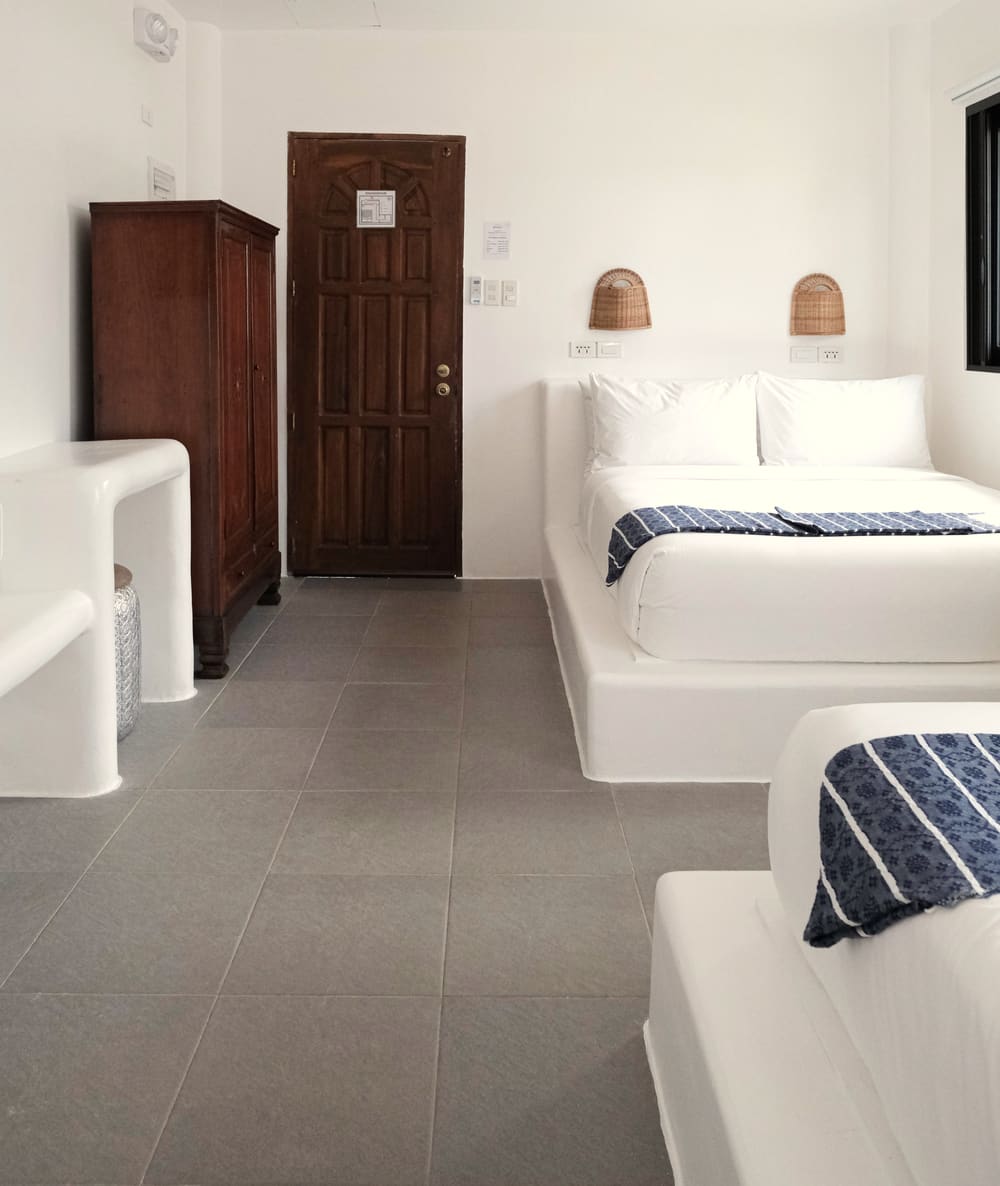Room with two double beds with blue striped runners, a dark wooden wardrobe, a wooden door and a white built-in desk.